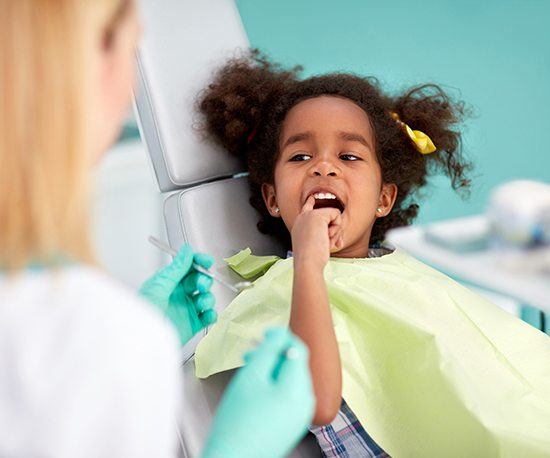 Child in dental chair pointing to smile
