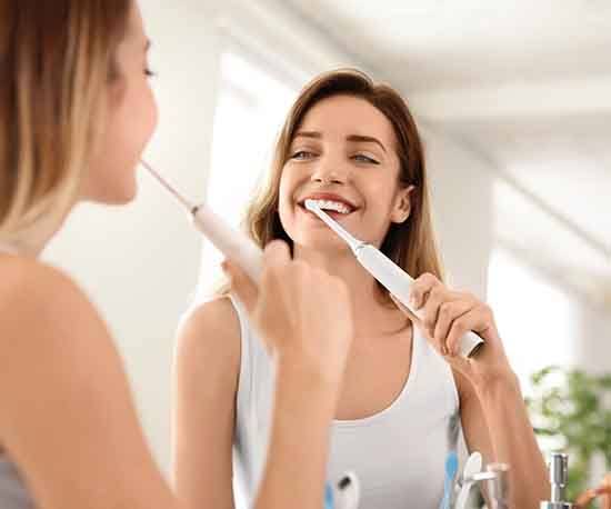 young woman brushing teeth with electric brush 