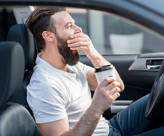 Man in car covering his mouth as he yawns