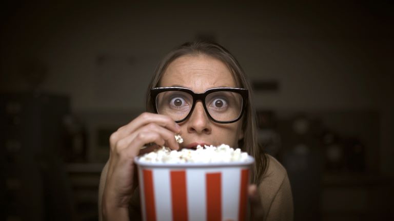 A scared looking woman hiding behind a bucket of popcorn.